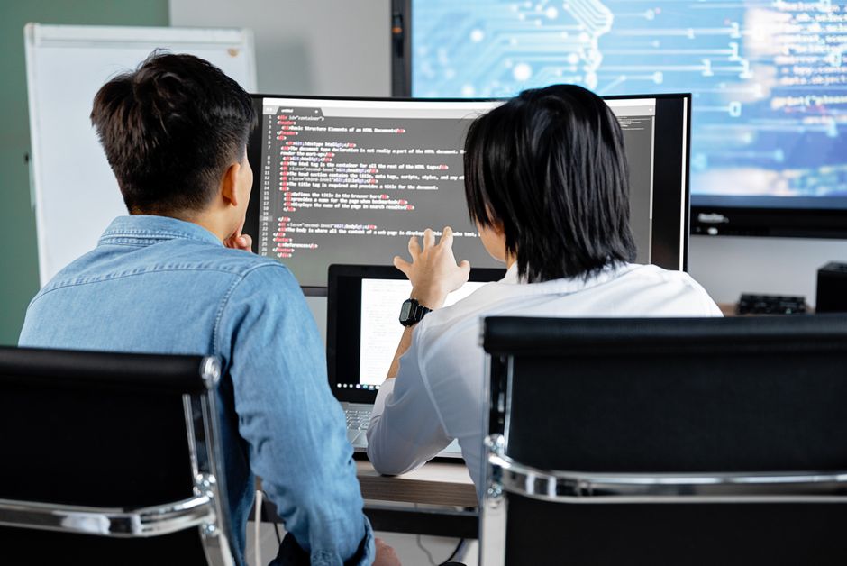 Dos desarrolladores trabajando juntos en una oficina, discutiendo código en una pantalla.
