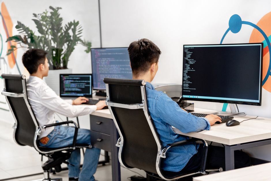 Dos desarrolladores programando en una oficina moderna con monitores grandes.