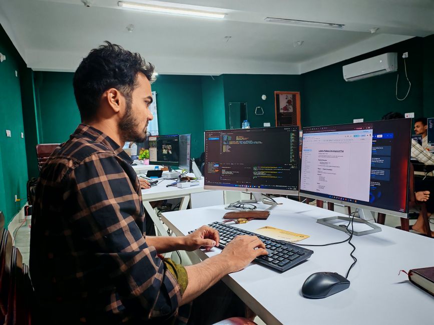 Un desarrollador de software trabajando en código en una configuración de doble monitor en una oficina moderna.