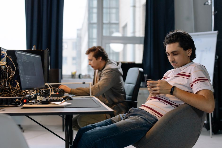 Dos hombres trabajando en una oficina moderna, uno en una computadora y el otro en un smartphone